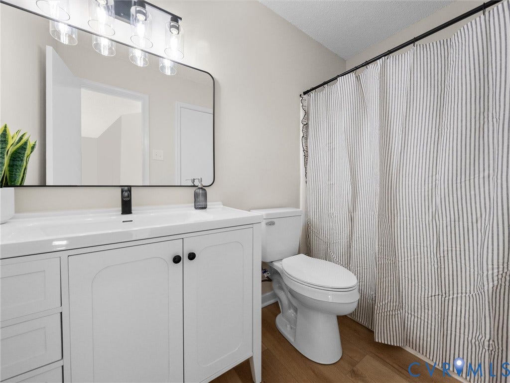 406 Alamosa Drive, Henrico, VA 23075 White vanity with integrated basin, matte black faucet, rounded rectangular mirror with a black frame, multi-bulb vanity light fixture, and wood-finish flooring