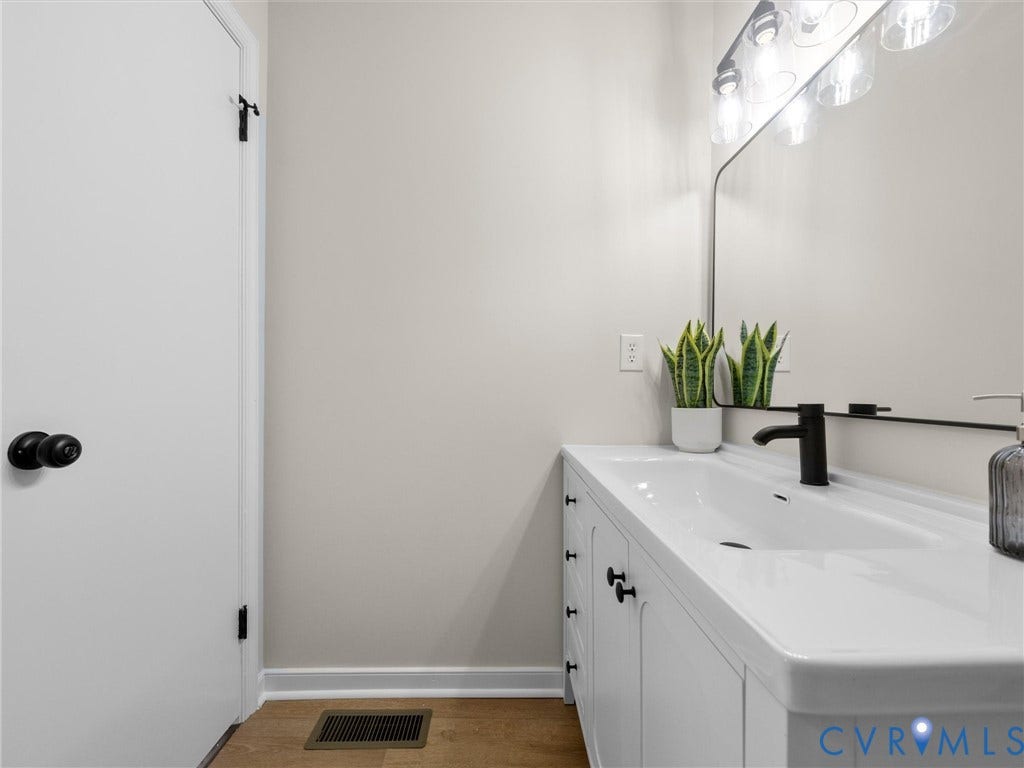 406 Alamosa Drive, Henrico, VA 23075 White vanity featuring an integrated sink, matte black faucet, and matte black hardware, paired with a rectangular wall-mounted mirror and multi-bulb vanity lighting