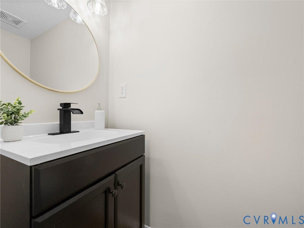 406 Alamosa Drive, Henrico, VA 23075 Dark cabinetry vanity with a white countertop, integrated sink, matte black faucet, and an oval mirror with a gold-finish frame