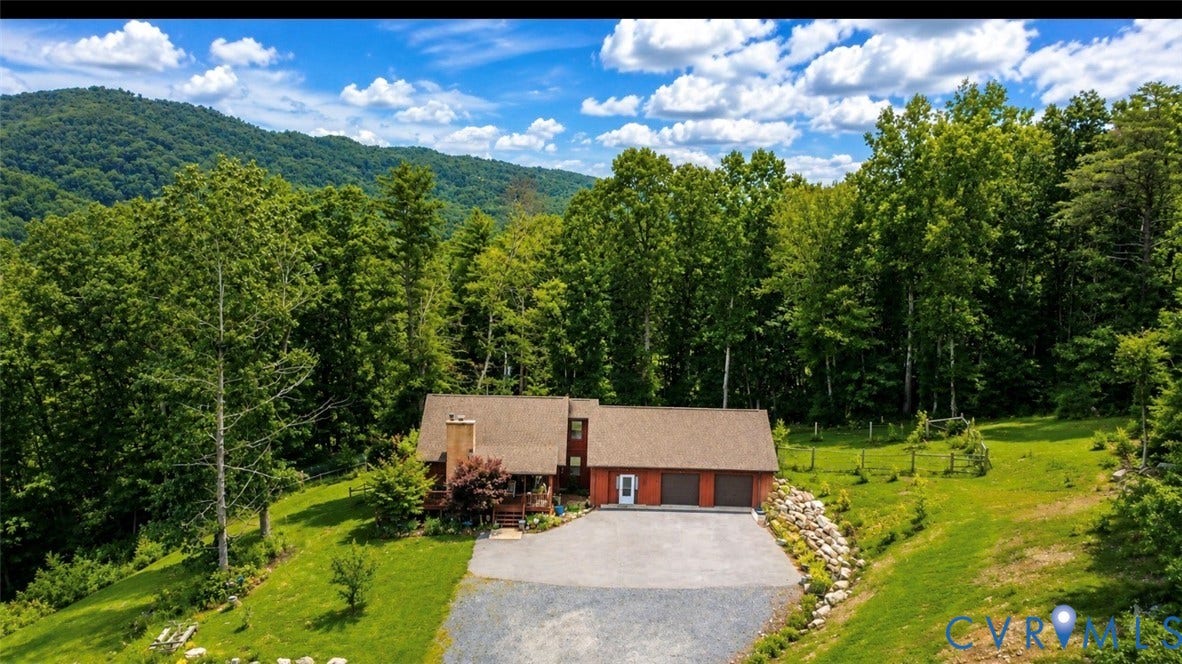 65 Cubbley Road, Hot Springs, VA 24445 Multi-level residence featuring a stone chimney, attached three-car garage, gravel driveway, and mountain backdrop