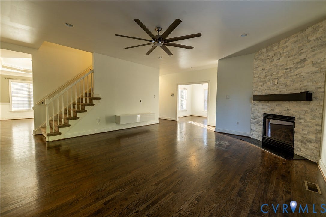 Interior featuring wood-finish flooring, a stone-veneer fireplace with a linear mantel, a wall-mounted floating console, recessed lighting, and a multi-blade ceiling fan