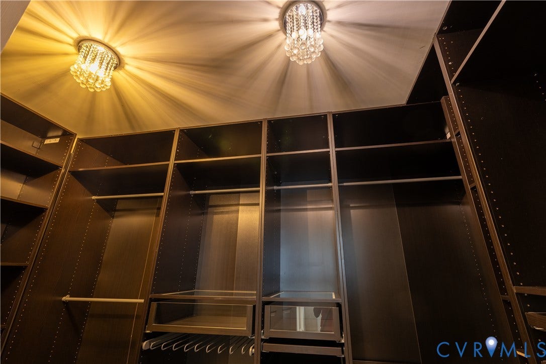 Custom dark wood-finish cabinetry featuring integrated shelving, hanging rods, and glass-front drawers, illuminated by dual crystal flush-mount light fixtures