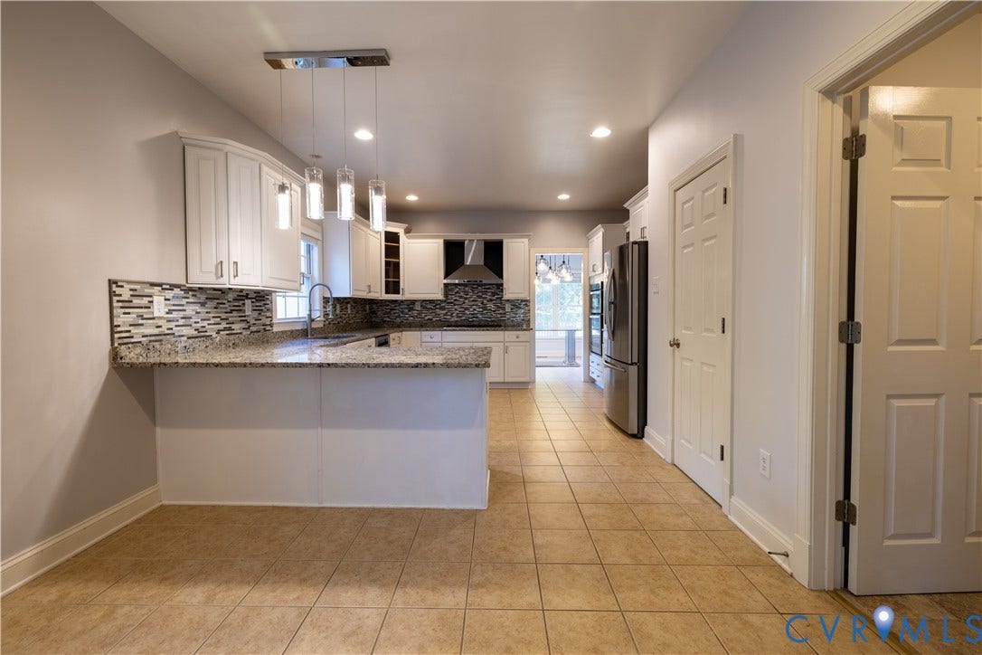 Kitchen featuring white cabinetry, stone countertops, multi-toned tile backsplash, stainless steel appliances, and multi-pendant lighting