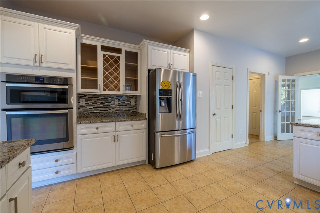 Kitchen featuring white shaker-style cabinetry, a built-in wine rack, stone-surfaced countertops, a mosaic tile backsplash, and stainless steel wall-mounted double ovens
