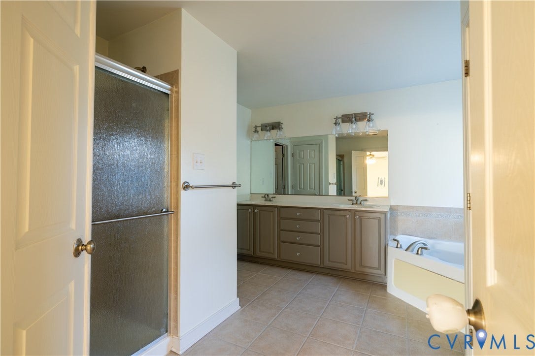 Bathroom featuring a dual-sink vanity with solid-surface countertops, a glass-enclosed shower, a built-in soaking tub with tile surround, and tile flooring
