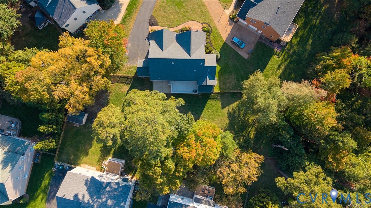 Aerial view featuring a multi-pitched roofline, expansive rear lawn, mature tree canopy, and a concrete patio