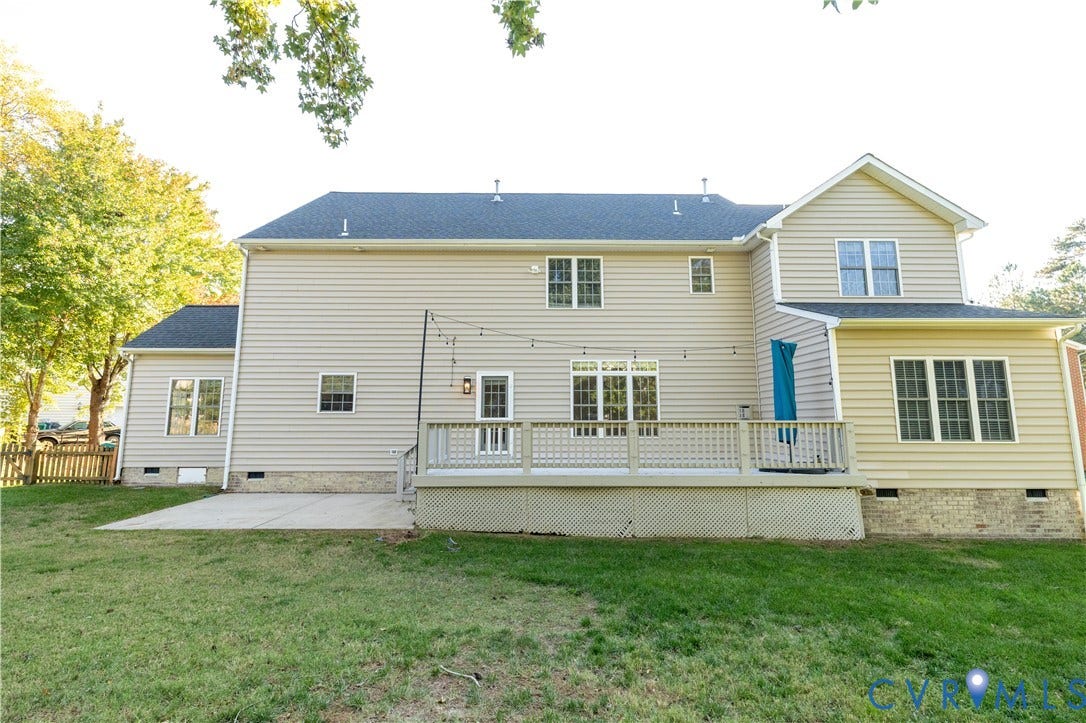 Two-story exterior featuring light-colored siding, a stone veneer foundation, a raised wooden deck with lattice skirting, and a poured concrete patio