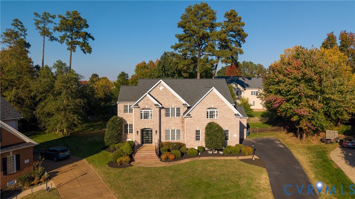 Multi-story brick exterior featuring a multi-gabled roofline, front-facing masonry steps, expansive lawn, mature trees, and a paved private driveway