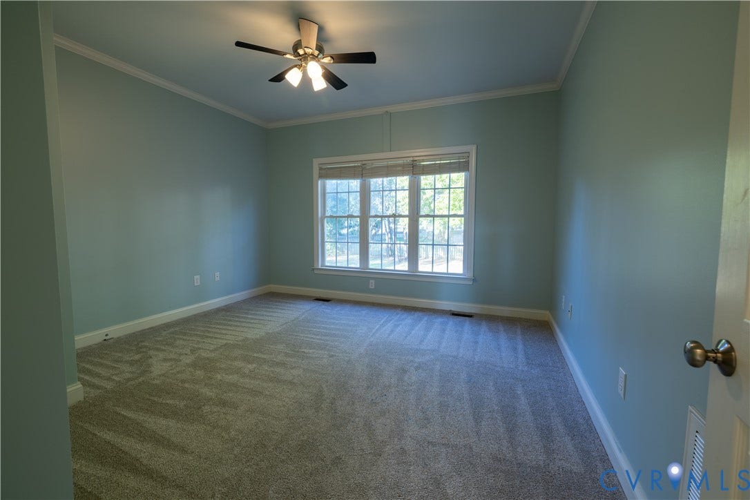 Spacious room featuring neutral carpeting, triple-pane window with blinds, crown molding, and a ceiling fan with integrated lighting