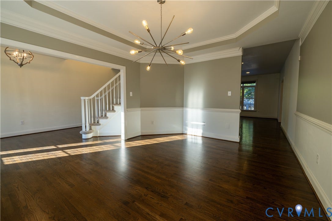 Tray ceiling with crown molding, wood-finish flooring, modern starburst chandelier, white chair rail wainscoting, and wooden staircase with white balusters