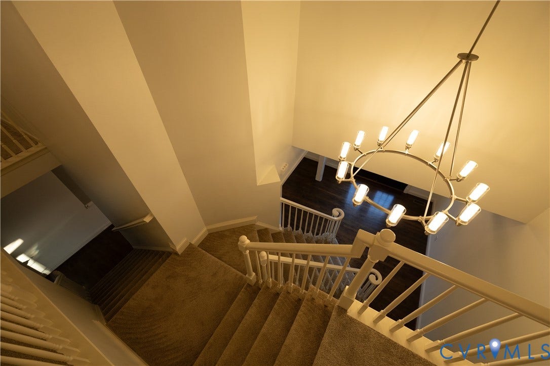 Staircase featuring carpeted steps, a white wooden railing with decorative balusters, and a tiered circular chandelier with metallic finish