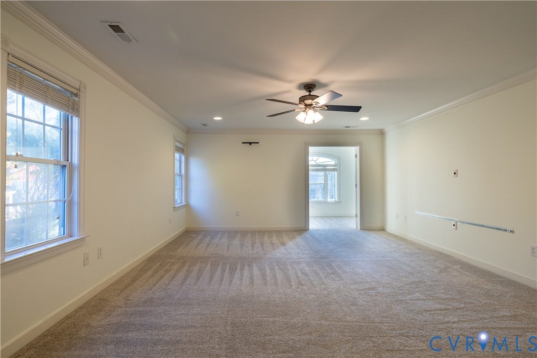 Neutral interior space featuring carpeted flooring, crown molding, double-hung windows with trim, and a ceiling fan with integrated lighting