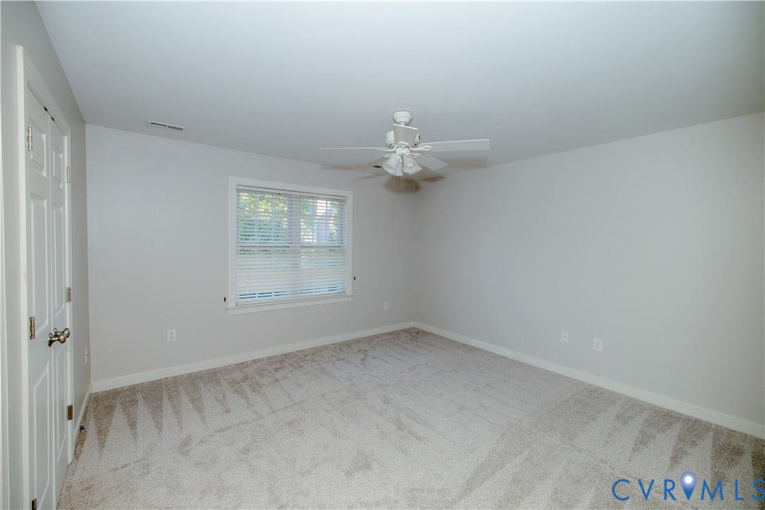 Neutral-toned interior space featuring wall-to-wall carpeting, a multi-blade ceiling fan with integrated lighting, and a window with horizontal blinds