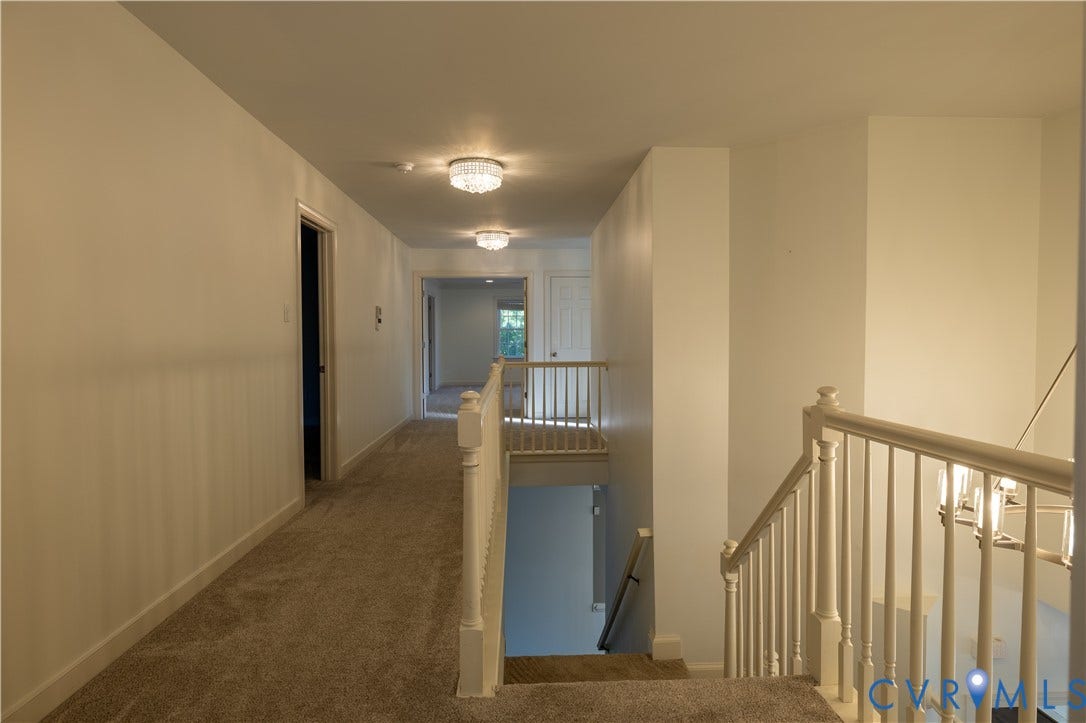 Hallway featuring wall-to-wall carpeting, white interior doors, decorative flush-mount ceiling lighting, and a white baluster railing