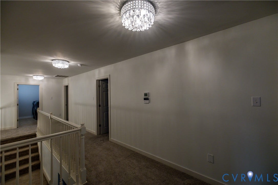 Hallway featuring multiple crystal-accented semi-flush mount light fixtures, carpeted flooring, and a wooden banister railing