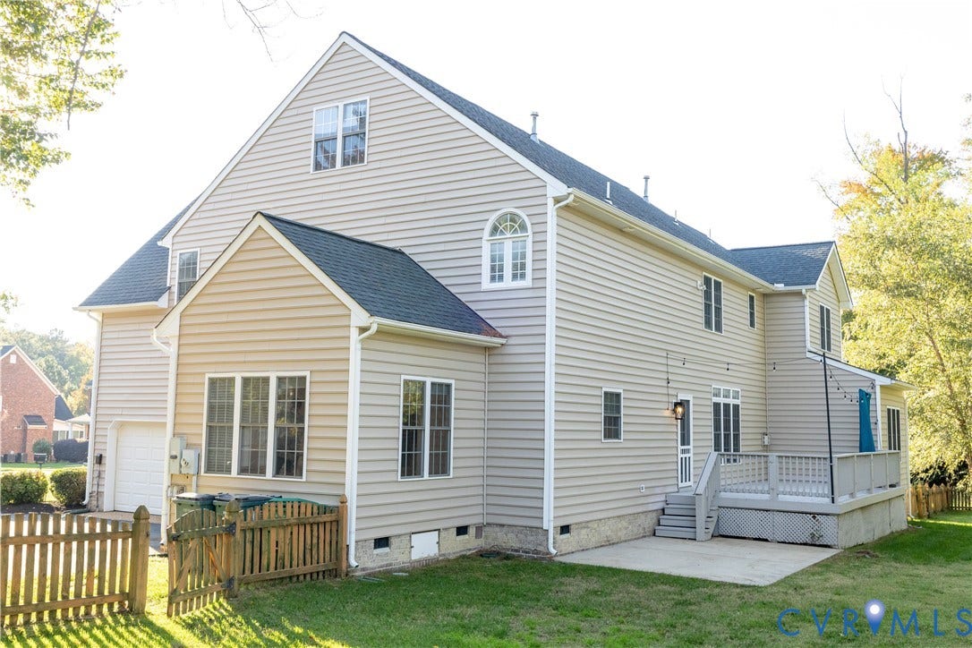 Two-story exterior featuring light-toned horizontal siding, a pitched asphalt shingle roof, raised wood deck, ground-level concrete patio, and a partially fenced yard