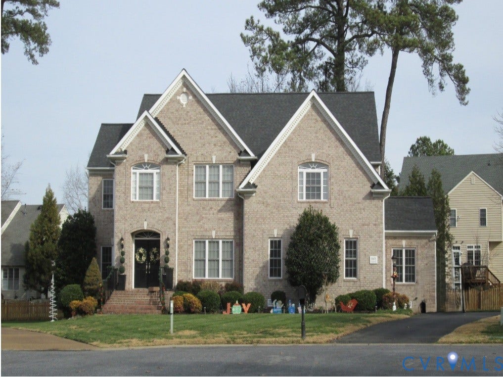 Multi-story brick exterior featuring a steeply pitched roofline, decorative gable trim, arched entryway, and double front doors