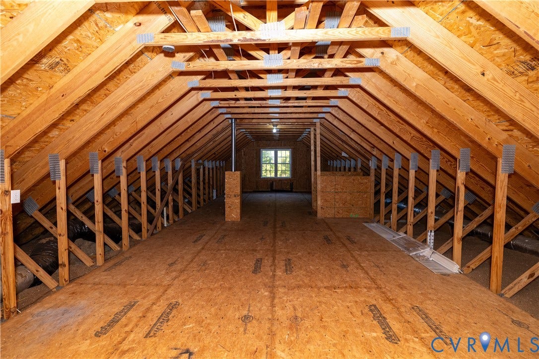 Unfinished attic space featuring exposed wood-truss construction, plywood subflooring, and a single pane window