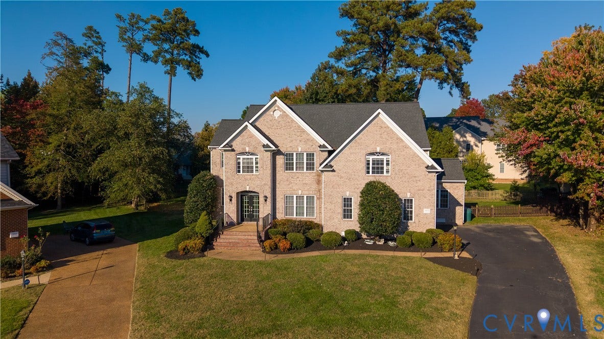 Multi-story brick exterior featuring a multi-gabled roofline, an arched entryway with brick stairs, and a paved driveway