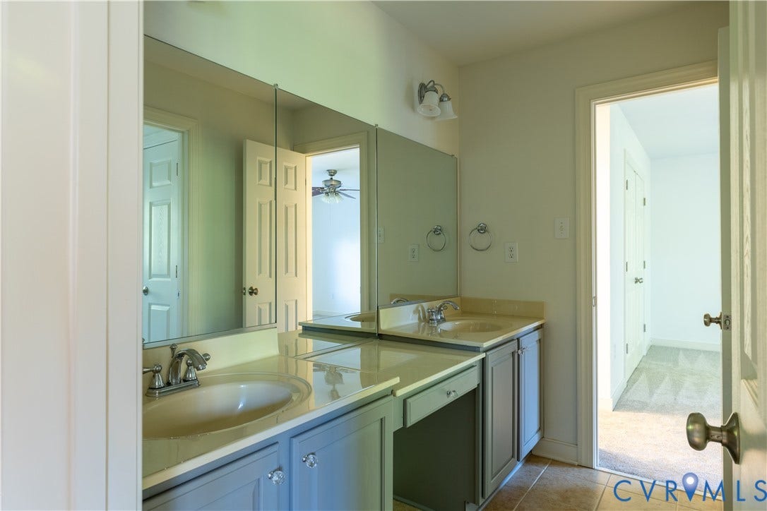 Bathroom featuring dual oval undermount sinks, solid surface countertops, full-width vanity mirror, and cabinetry with integrated drawer storage