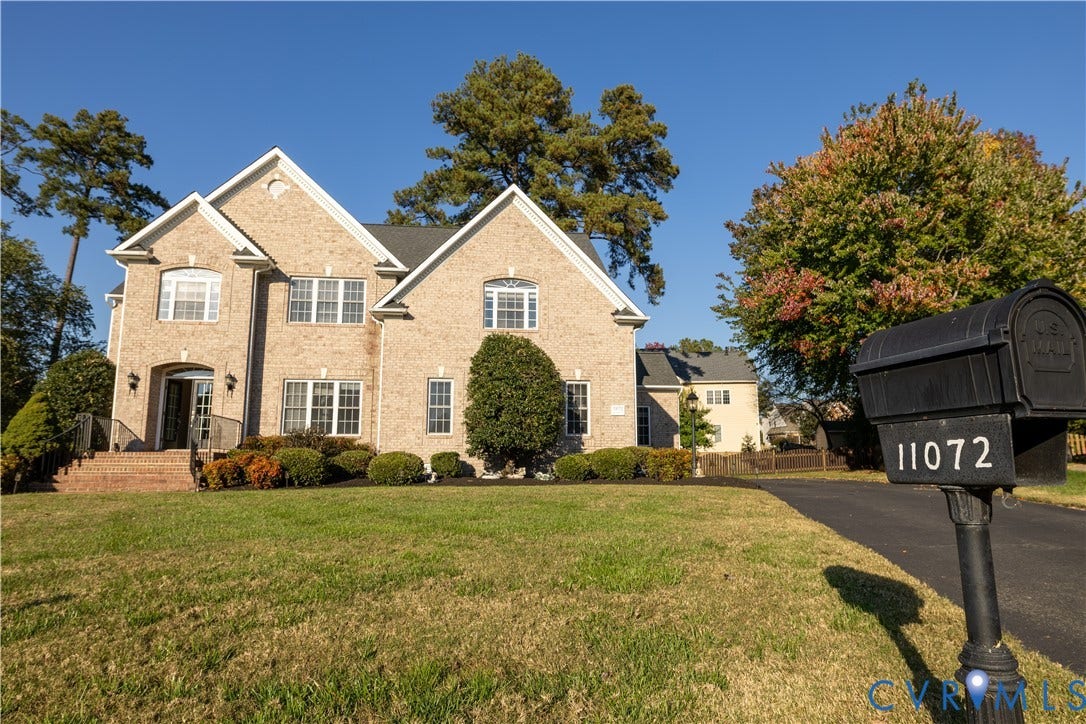 Two-story brick exterior featuring a multi-gabled roofline, an arched entryway with stone steps, and an asphalt driveway