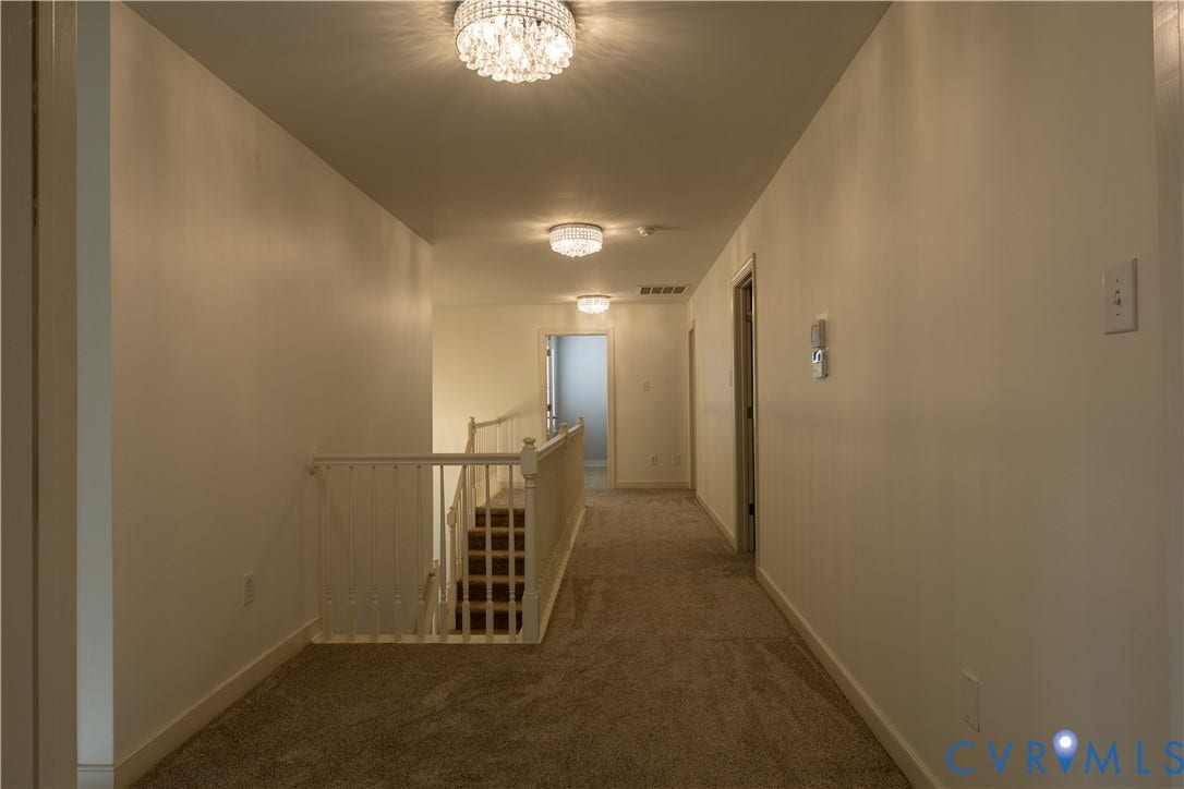 Hallway featuring neutral wall-to-wall carpeting, white interior doors, and three circular crystal-accented flush-mount light fixtures, complemented by a white wooden balustrade staircase