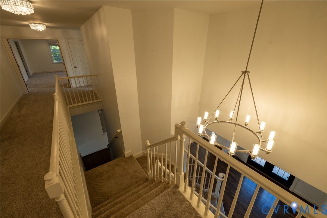 Multi-level staircase featuring neutral carpeting, white balustrade railing, and a tiered circular pendant light fixture