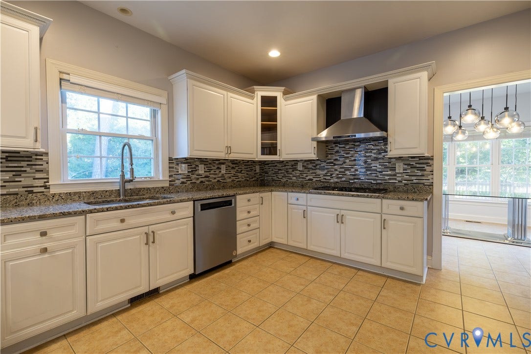 Kitchen featuring white shaker-style cabinetry, stone countertops, a multi-tonal glass tile backsplash, stainless steel appliances, and ceramic tile flooring