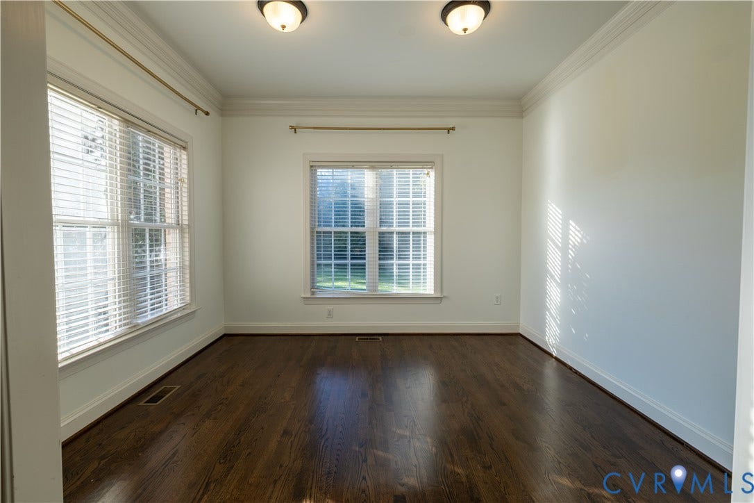 Dark wood-finish flooring featuring crown molding, dual flush-mount light fixtures, and multiple windows with horizontal blinds