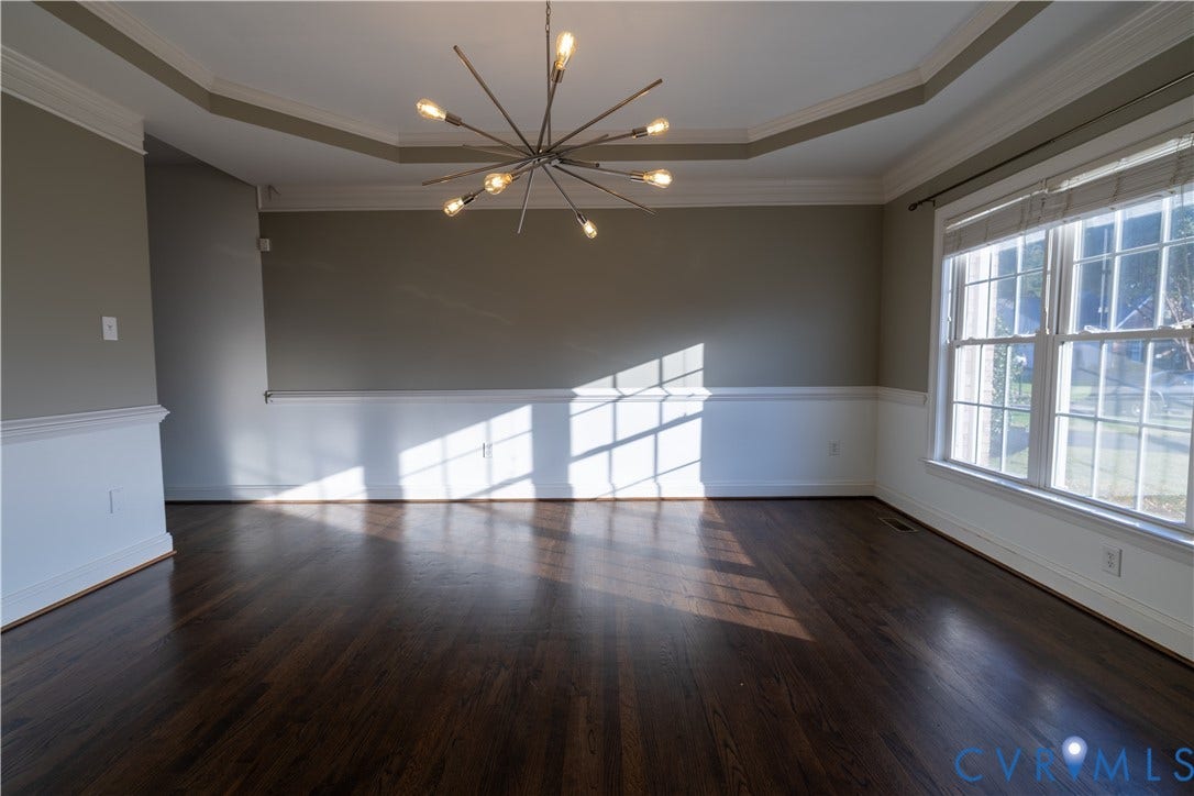 Tray ceiling featuring crown molding, dark-stained wood-finish flooring, white chair rail wainscoting, and a multi-arm geometric chandelier