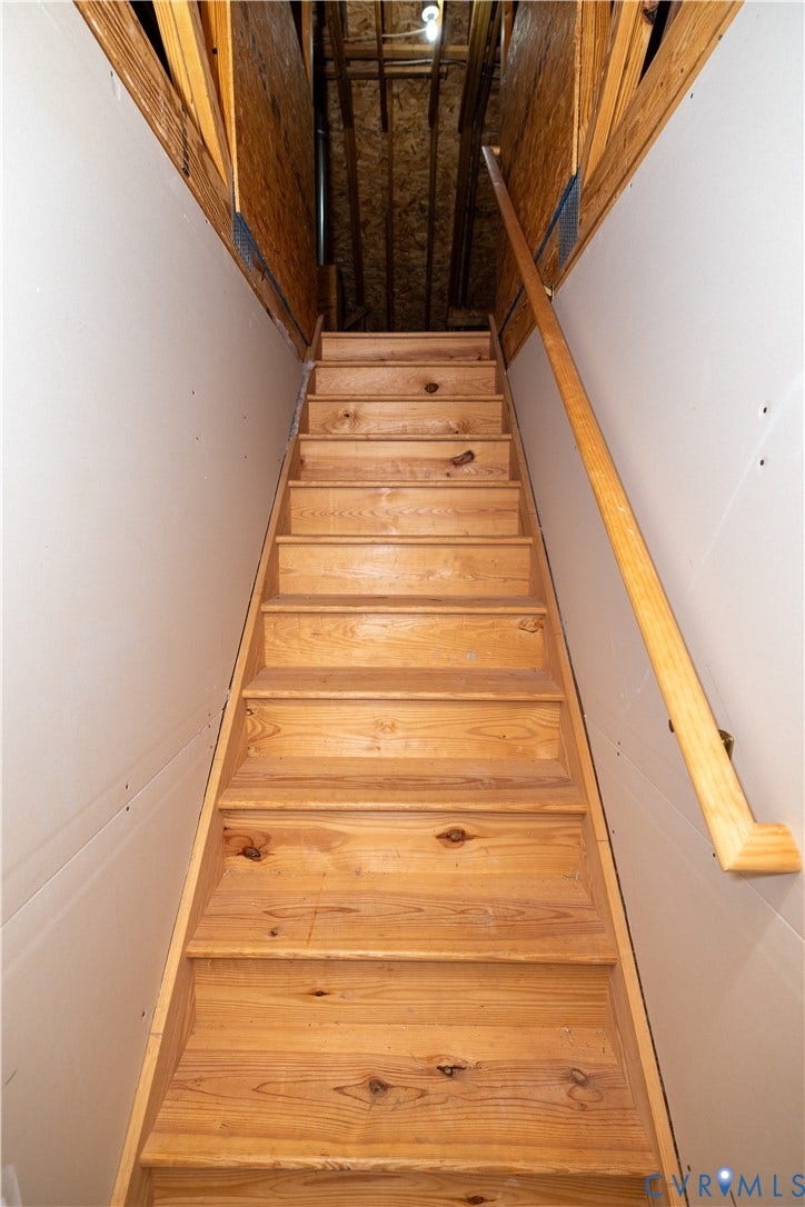 Staircase featuring natural wood treads, exposed wooden framing, and a mounted wooden handrail