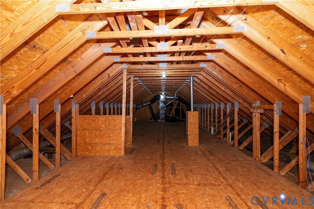 Attic space featuring exposed wooden trusses, metal gusset plates, subfloor decking, and mechanical components
