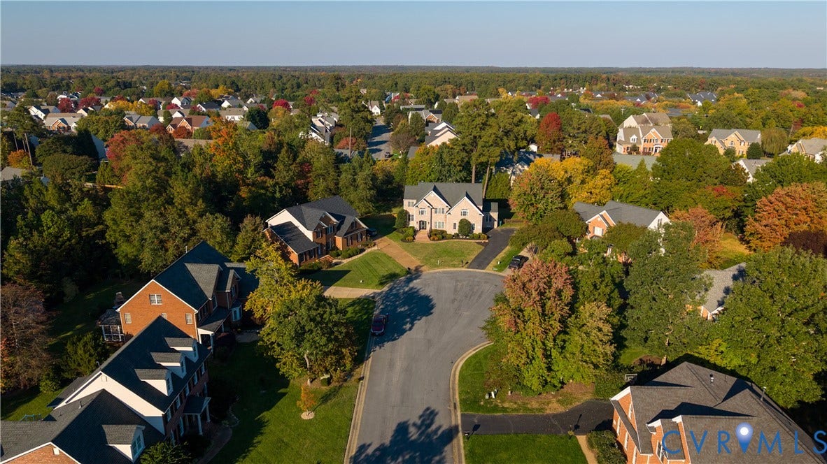 Aerial perspective of a multi-level suburban residence featuring a multi-gabled roofline, an expansive manicured lawn, and mature canopy trees situated along a paved cul-de-sac