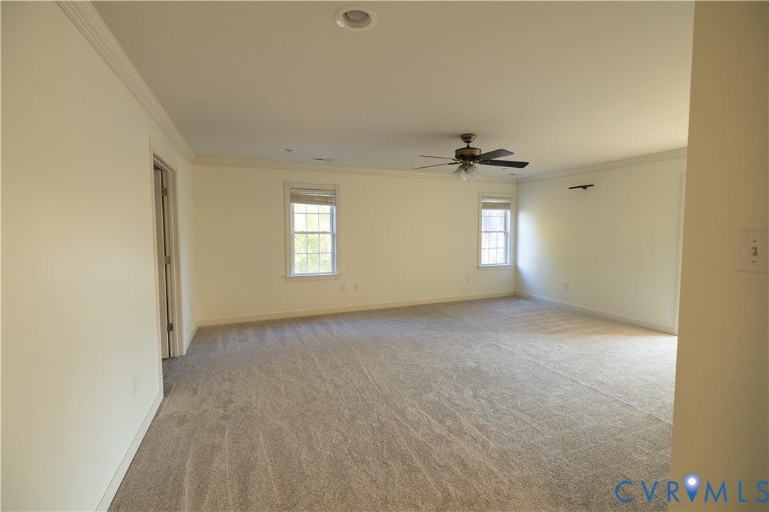 Spacious room featuring neutral carpeting, crown molding, multi-pane windows, and a ceiling fan with integrated lighting