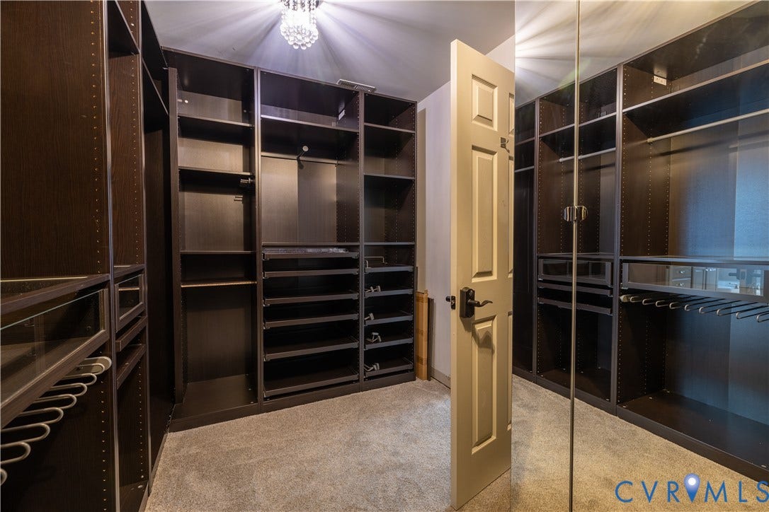 Custom walk-in closet featuring extensive dark-finish built-in shelving, integrated garment hanging rods, dedicated storage drawers, a full-length mirrored door, and a crystal-style ceiling light fixture