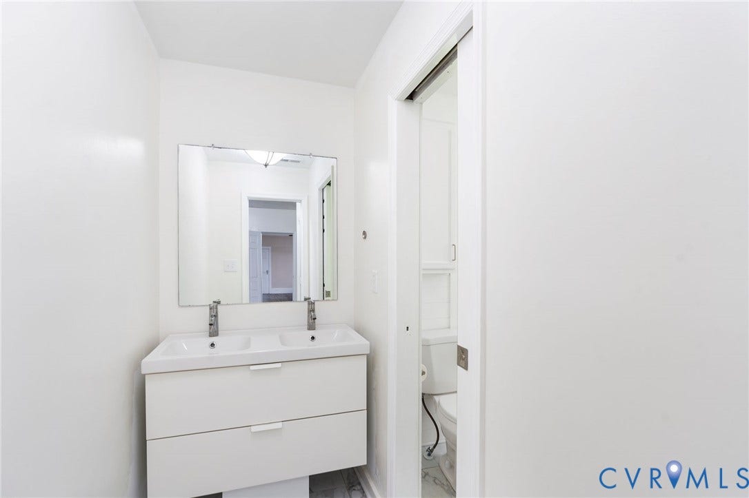 14043 Jefferson Highway, Louisa, VA 23024 Floating double vanity featuring a white composite countertop, integrated dual sinks, chrome faucets, and two storage drawers, paired with a frameless rectangular mirror and sliding door entry