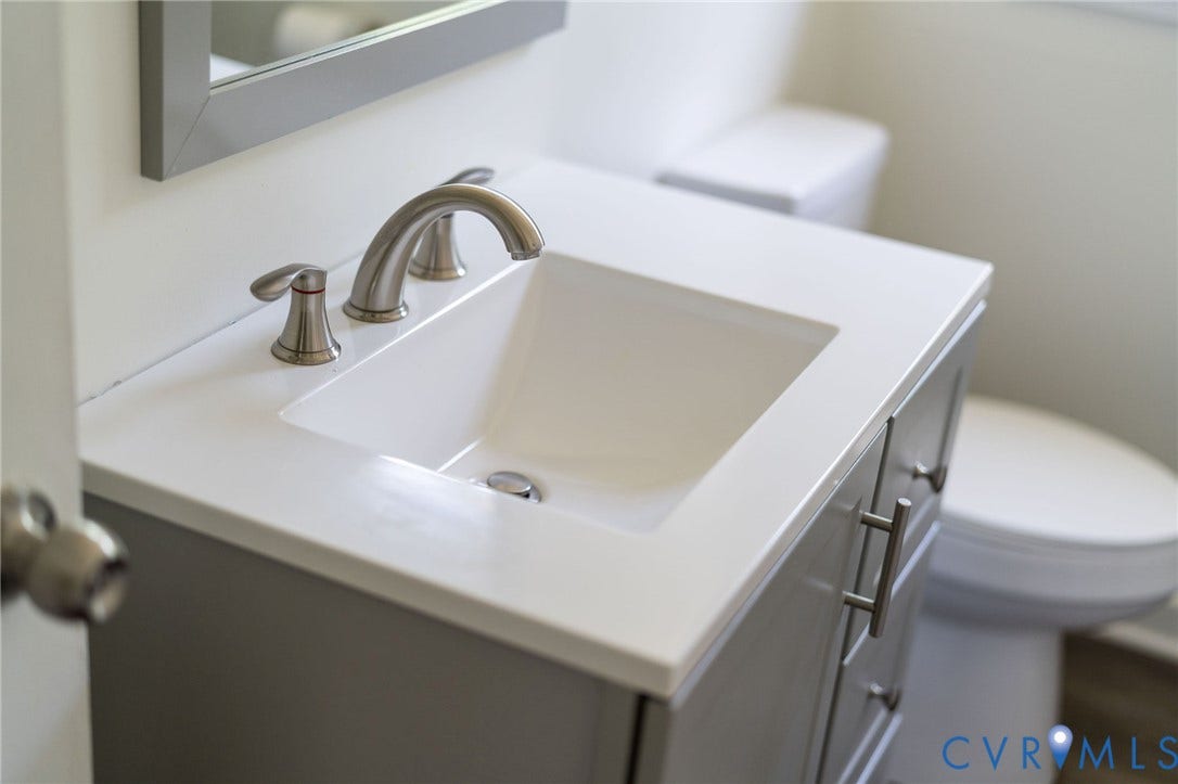 14043 Jefferson Highway, Louisa, VA 23024 Grey vanity cabinet featuring a white countertop with an integrated rectangular basin, brushed-nickel widespread faucet, and metal hardware