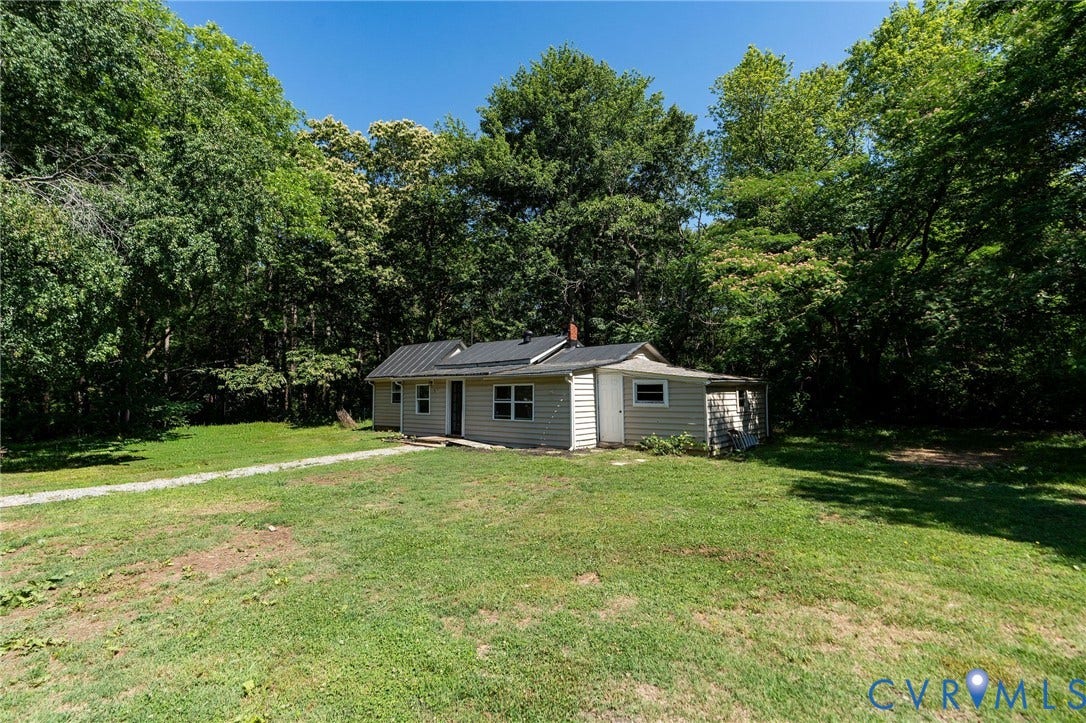 14043 Jefferson Highway, Louisa, VA 23024 Single-story exterior featuring horizontal siding, a dark metal roof, and a gravel driveway situated on a tree-lined lot