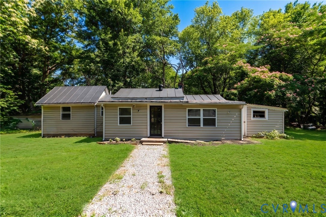 14043 Jefferson Highway, Louisa, VA 23024 Single-story residence featuring light-toned horizontal siding, a dark metal roof, a gravel walkway, and mature perimeter trees