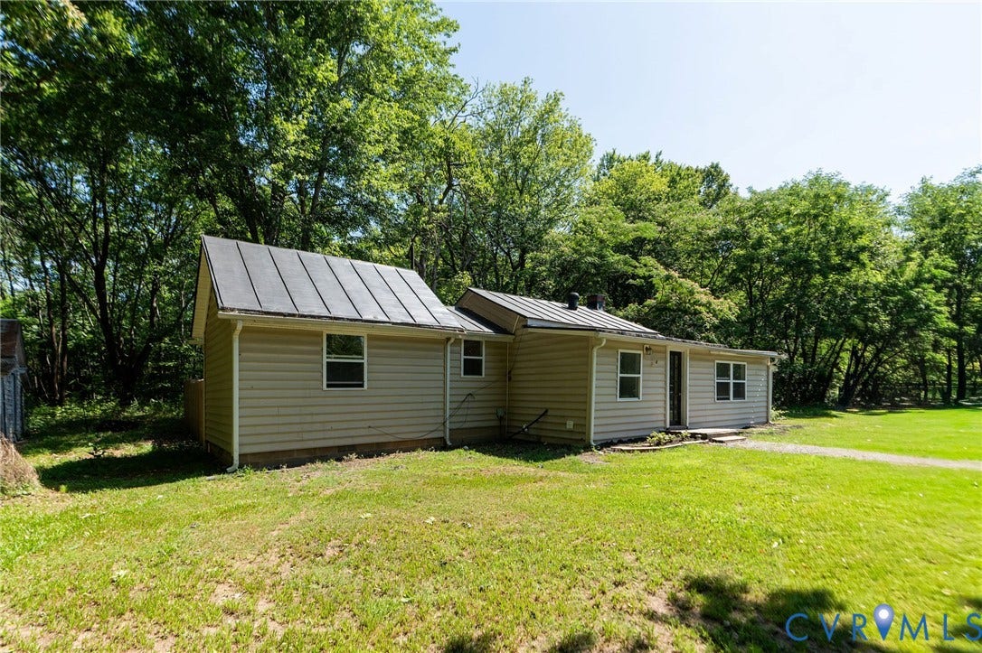14043 Jefferson Highway, Louisa, VA 23024 Single-story exterior featuring light-toned horizontal siding, a dark metal roof, and multiple window placements on a large grass lot with mature trees