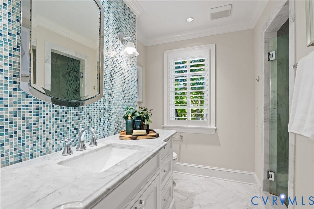 11429 Barrington Bridge Court, Henrico, VA 23233 Custom vanity featuring a natural stone countertop, undermount sink, and polished chrome hardware, accented by a blue glass mosaic tile backsplash, framed wall mirror, and white plantation shutters