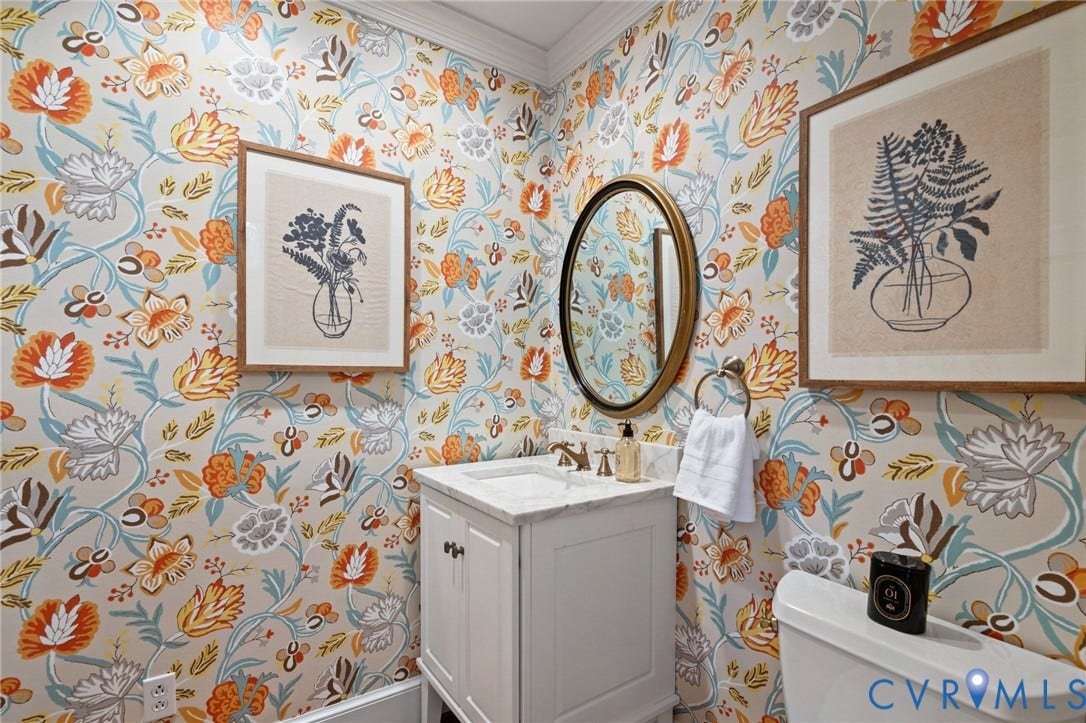 11429 Barrington Bridge Court, Henrico, VA 23233 Powder room featuring floral patterned wallpaper, white vanity with stone countertop, oval gold-framed mirror, and metallic faucet hardware