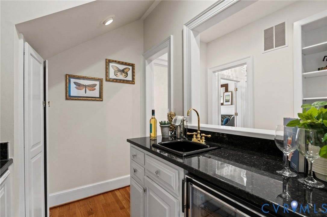 11429 Barrington Bridge Court, Henrico, VA 23233 Wet bar featuring dark stone countertops, a black undermount sink with brass finish hardware, custom white cabinetry, and built-in shelving