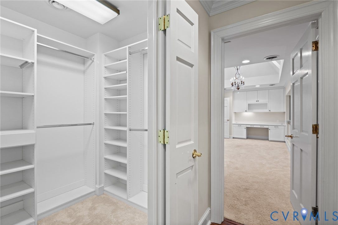 11429 Barrington Bridge Court, Henrico, VA 23233 Walk-in closet featuring white custom built-in shelving, hanging rods, and carpeted flooring, opening to a space with built-in cabinetry and a desk area