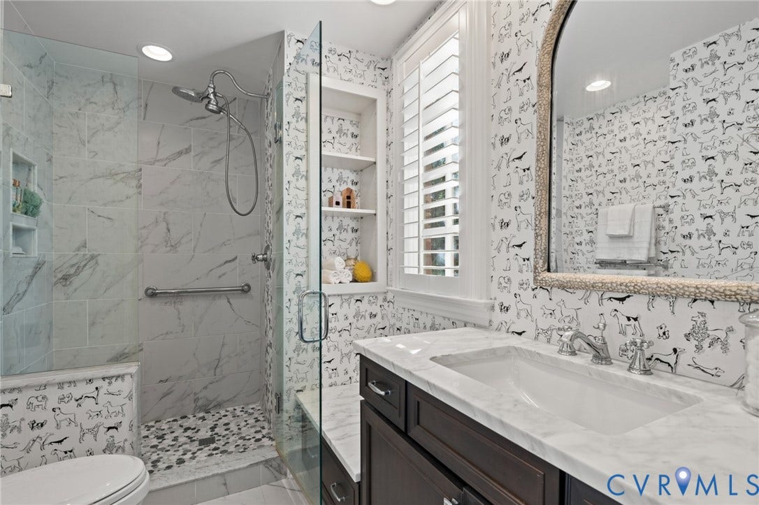 11429 Barrington Bridge Court, Henrico, VA 23233 Bathroom featuring stone-finish wall tile, a walk-in shower with a pebble-style floor, a built-in storage niche, stone-top vanity, and plantation shutters