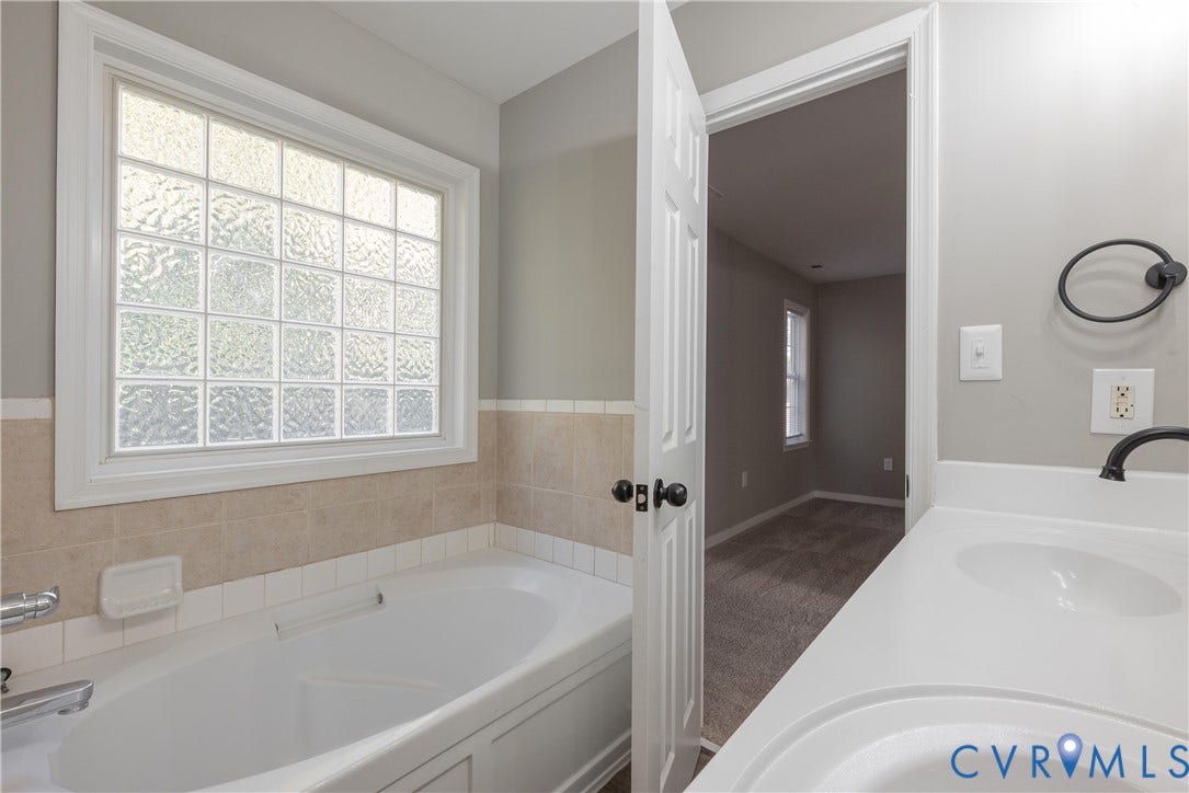 7009 Summers Trace Court, Chesterfield, VA 23832 Soaking tub with tile surround, glass block privacy window, dual-basin vanity with solid-surface countertop, and matte black hardware fixtures