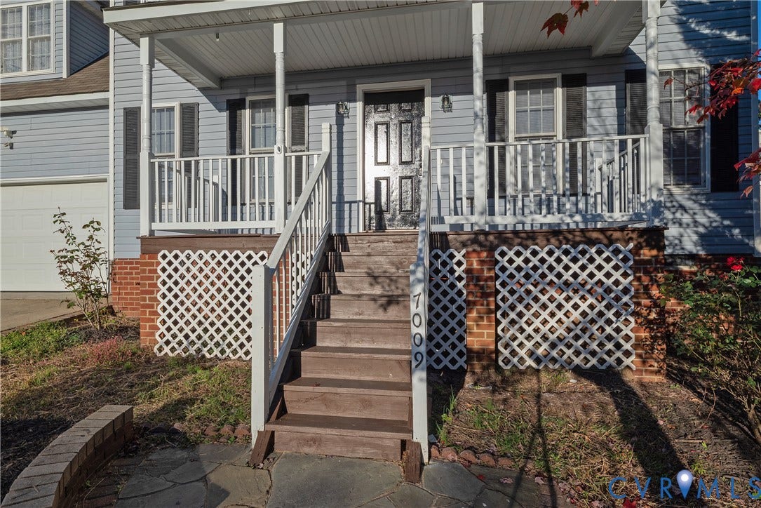 7009 Summers Trace Court, Chesterfield, VA 23832 Front exterior featuring blue horizontal siding, a covered porch with white railing, brick foundation skirting, wood-finish stairs, and a flagstone patio