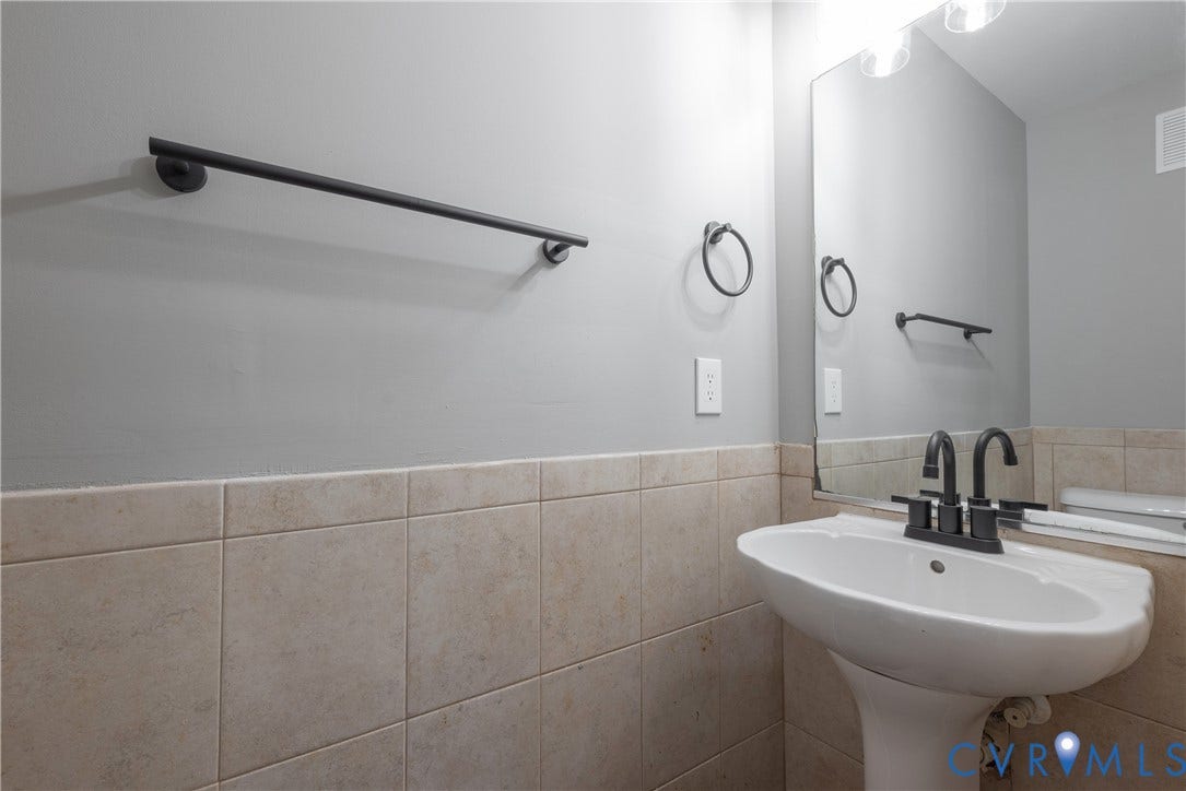 7009 Summers Trace Court, Chesterfield, VA 23832 Powder Room Pedestal sink with a matte black faucet, wall-mounted mirror, ceramic tile wainscoting, and matte black towel hardware