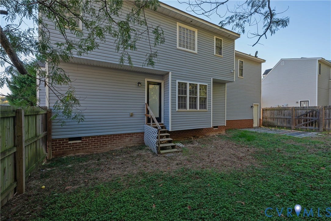 7009 Summers Trace Court, Chesterfield, VA 23832 Rear exterior featuring horizontal lap siding, brick foundation, multi-pane windows, and a wood staircase leading to a rear entrance, enclosed by wood privacy fencing