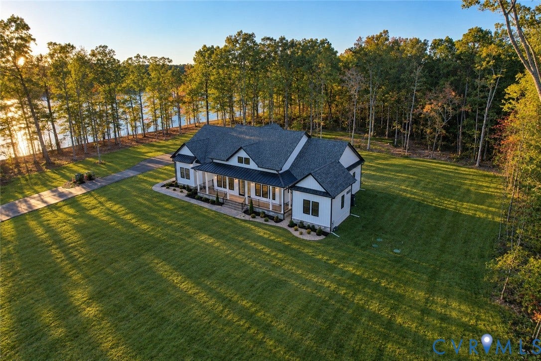 Contemporary residence featuring a multi-gabled roofline, covered front porch, asphalt shingle roofing, paved driveway, and expansive lawn situated on a waterfront lot
